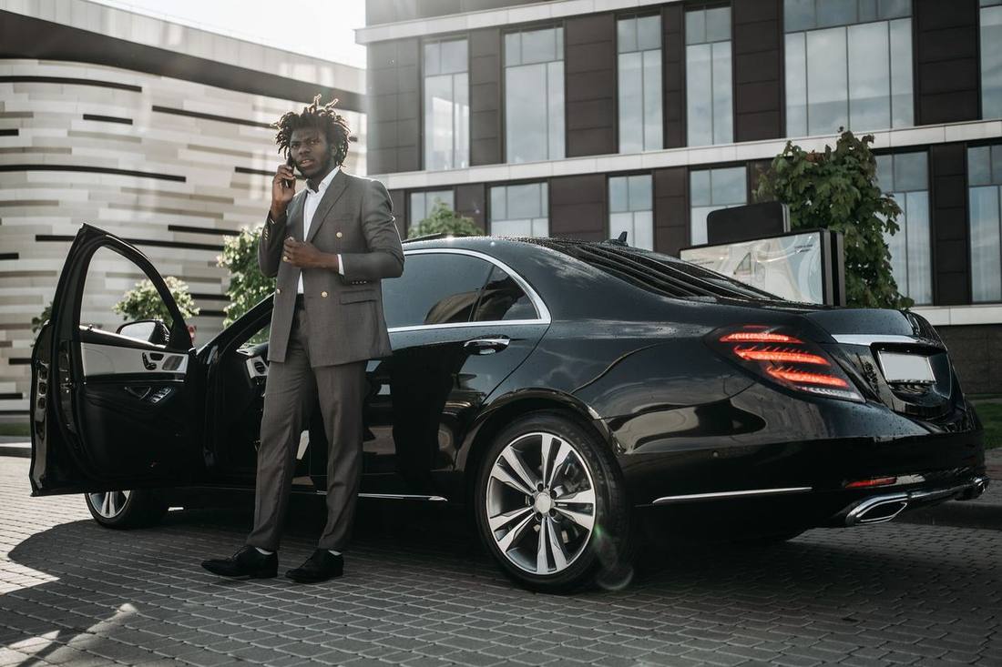 A chauffeur waiting beside a black sedan on a Yorkville side street with the vehicle's lights on