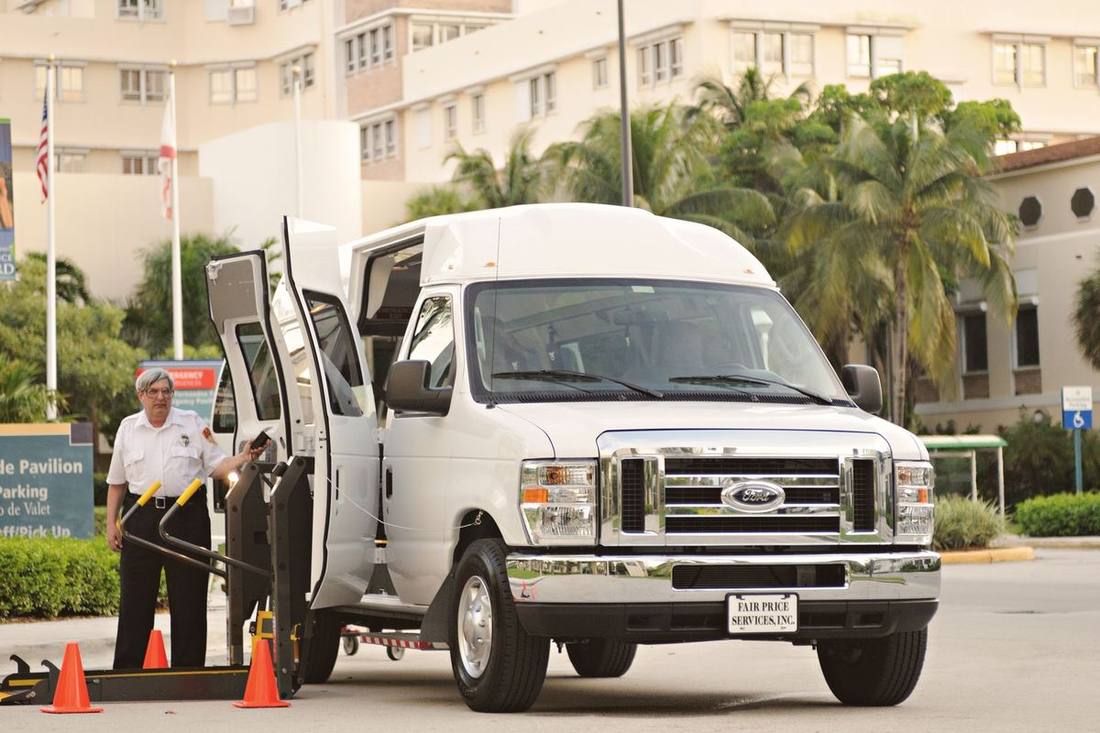 A chauffeur securing a wheelchair with tie-downs inside an accessible van