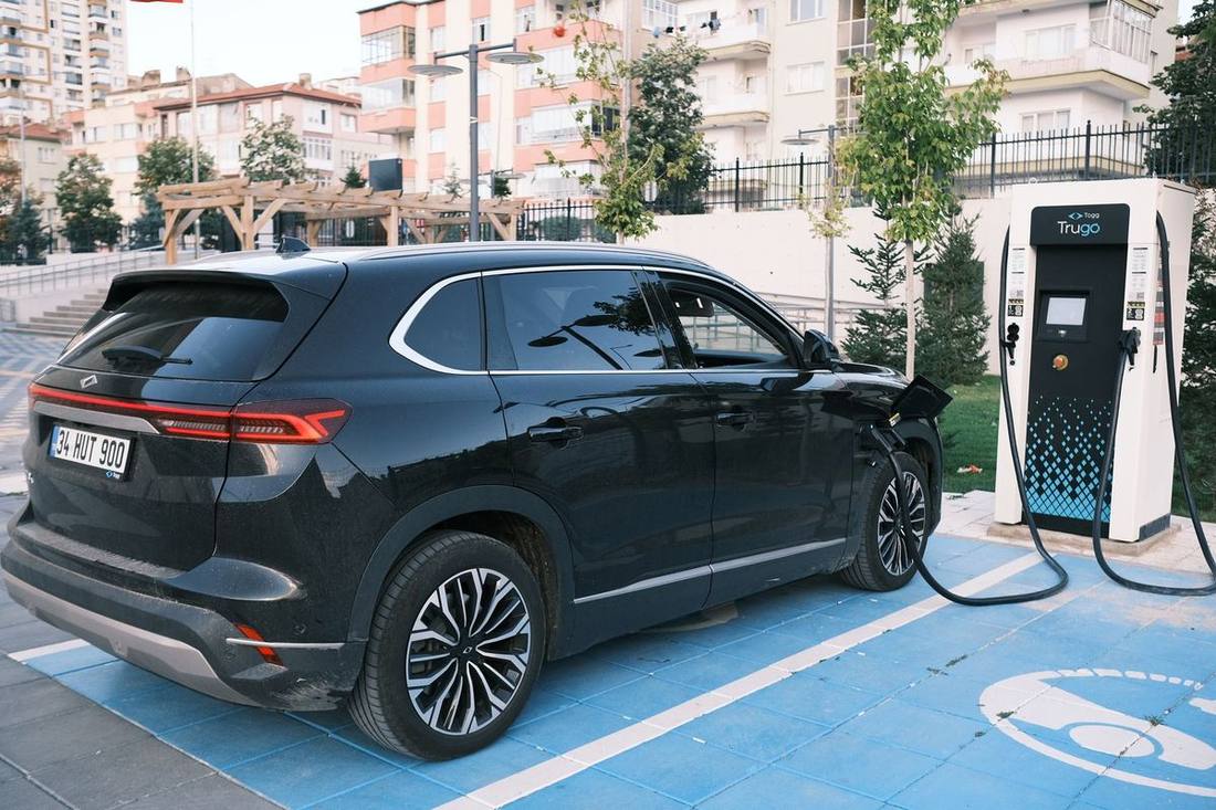 An electric black SUV charging at a fleet depot with a row of hybrid sedans behind it