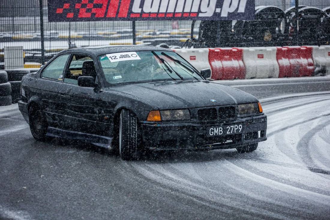 A black sedan on a wet closed-course skid pad with cones during a chauffeur training day