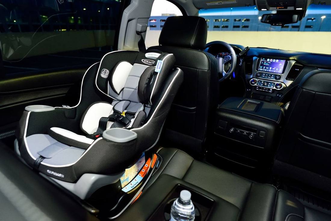 A rear-facing infant seat installed on its base in the rear of a black sedan with the tether and belt path visible
