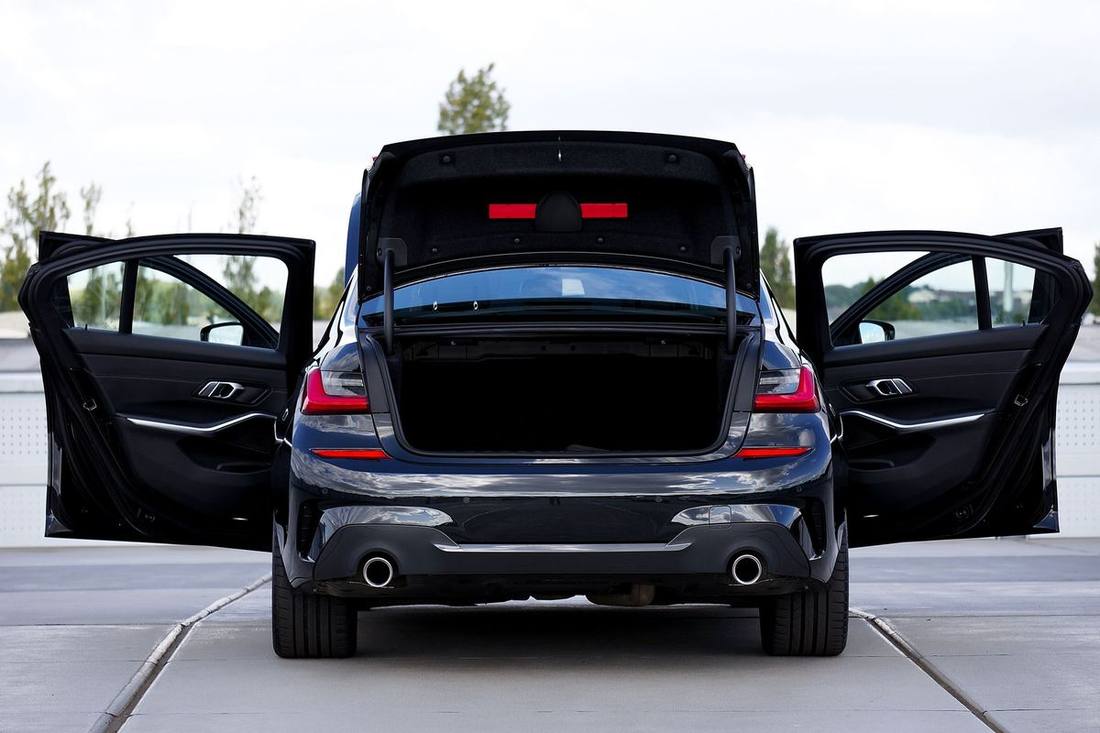 A black luxury sedan on a lift in a fleet's maintenance bay with a mechanic inspecting the air suspension