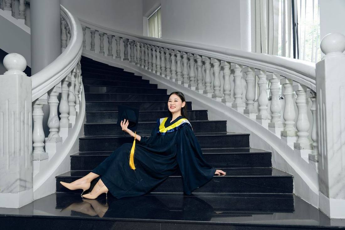 A graduate in gown and hood stepping from a black SUV in front of a university hall