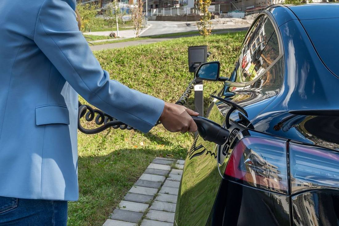 A chauffeur connecting a charging cable to a black electric SUV in a fleet depot at night