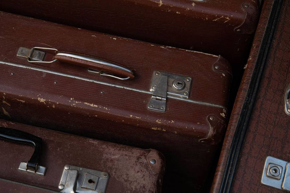Suitcases of three sizes lined up beside the open trunk of a black sedan at a Toronto curb
