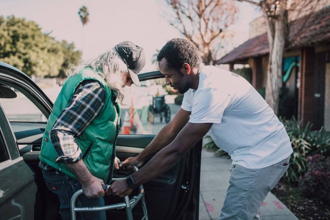 A chauffeur helping a passenger with a walker into a black SUV
