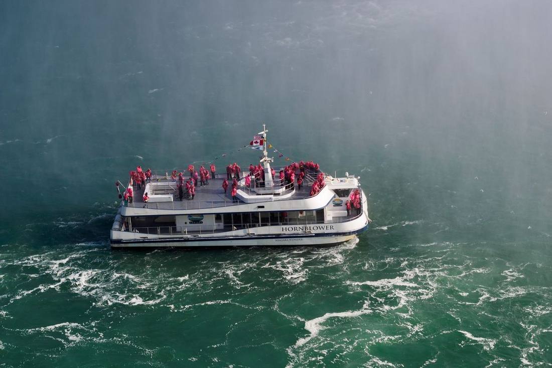 A chauffeur holding an SUV's door at the Table Rock Centre lay-by with passengers in ponchos returning from the falls
