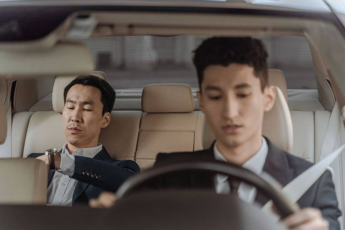 A chauffeur checking a child seat's installation and a rear seat belt before a pickup