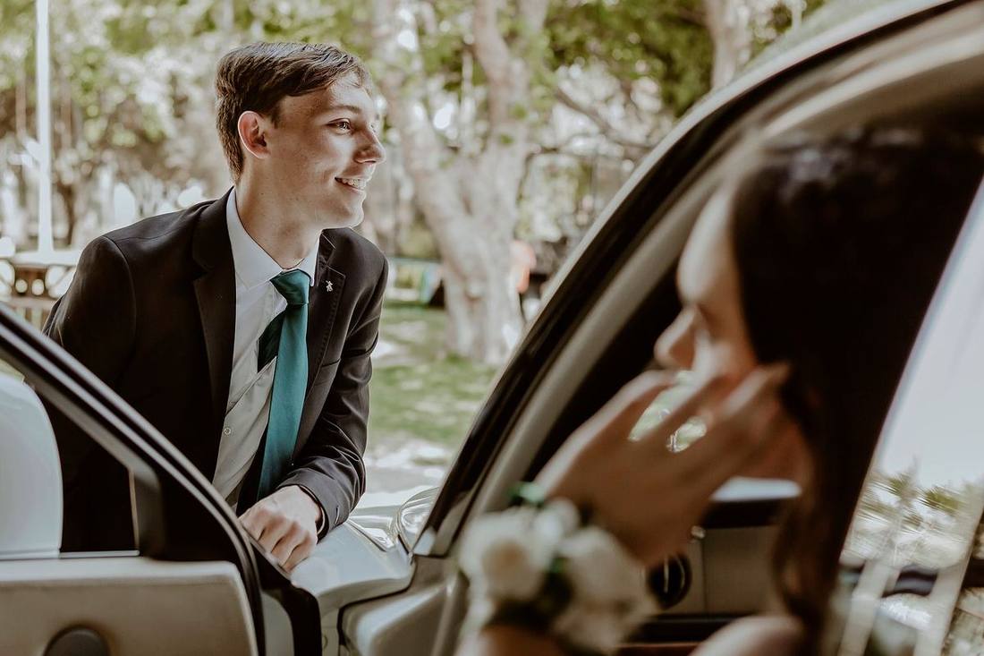 A chauffeur holding a stretch limousine's door for a prom group at a venue's entrance