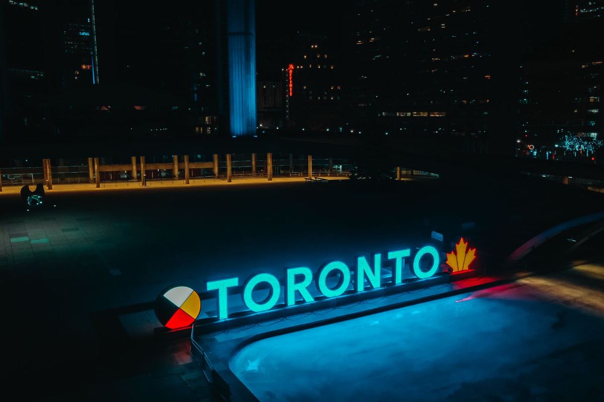 Nathan Phillips Square lit for a winter festival with skaters on the rink and a black SUV on Queen Street