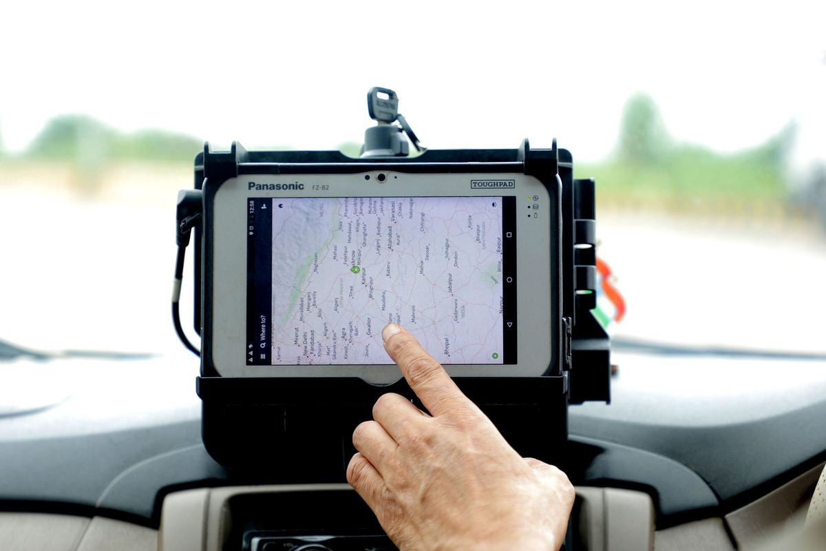 A chauffeur checking a live traffic map on a tablet in a parked black car at dawn before the morning peak