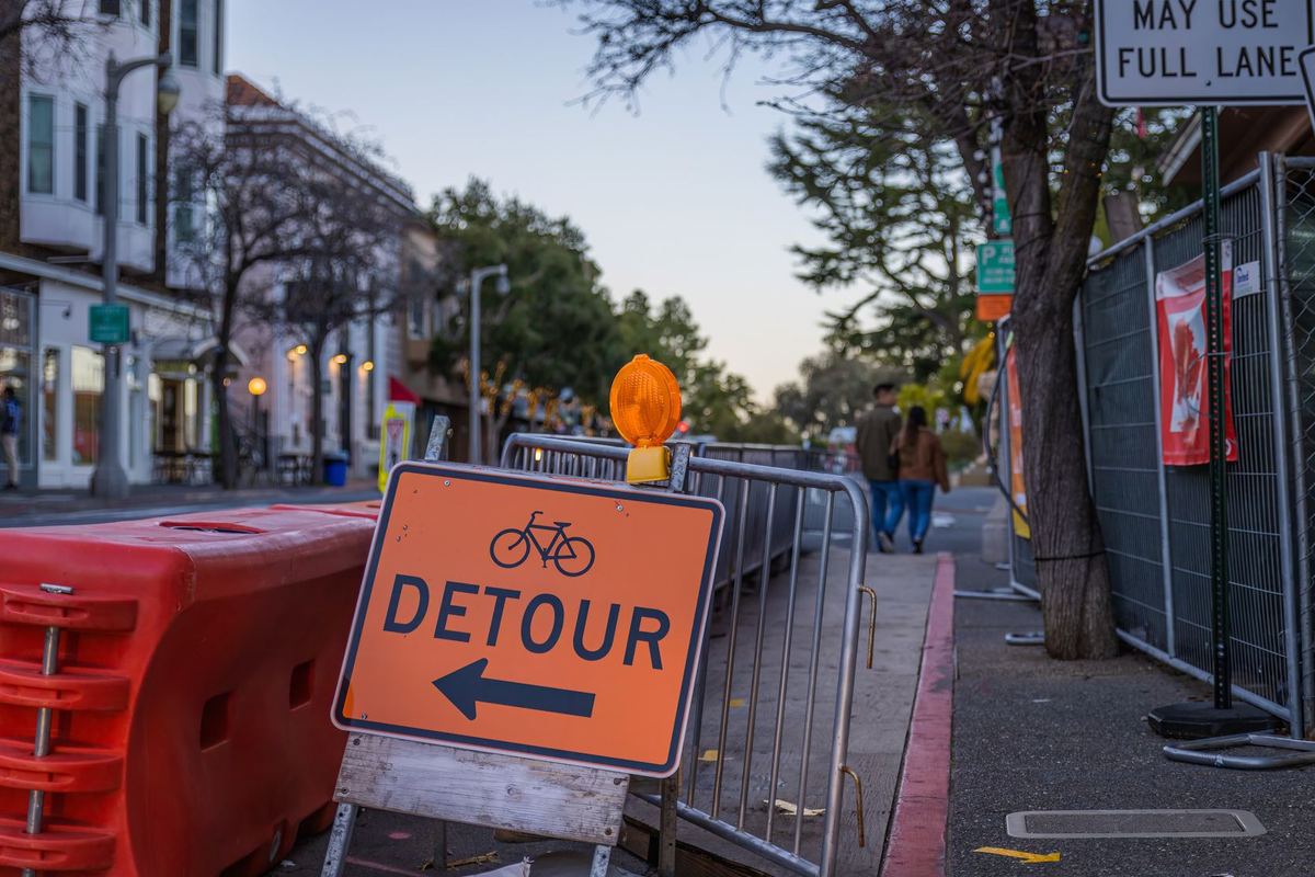 A black sedan taking a detour past orange construction barriers and a lane closure on a Toronto downtown street in summer
