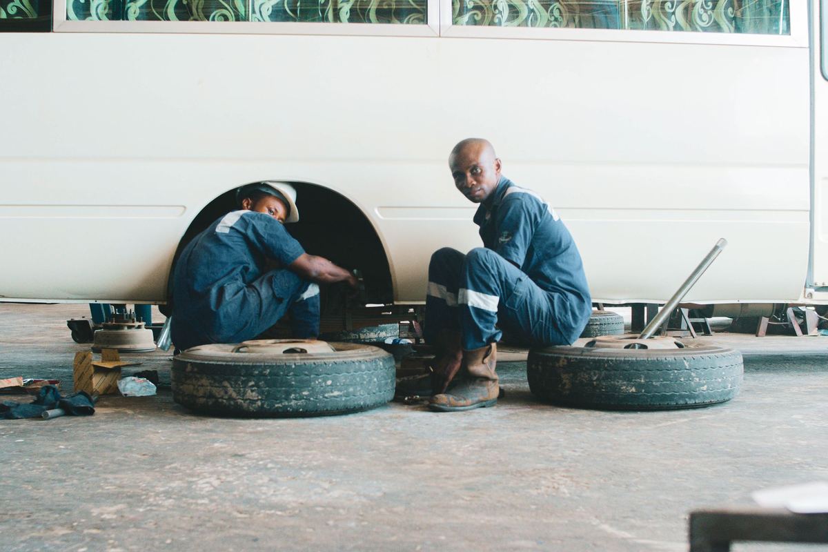 A fleet technician fitting a winter tire on a black SUV's rim in a depot with snow visible outside