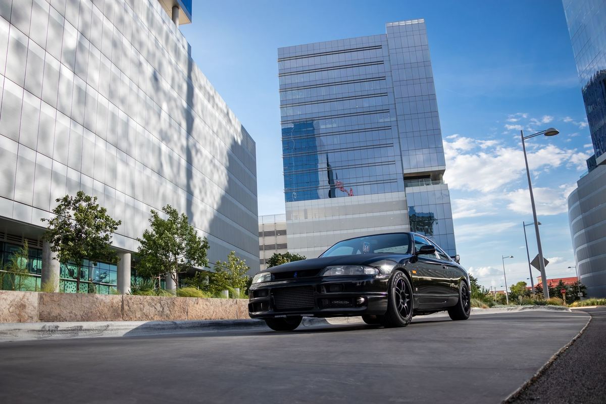 A black sedan waiting beneath a glass tower